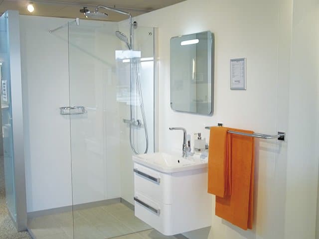 Et billede af en brusebad, håndvask, spejl og et orange håndklæde hængende ved siden af
